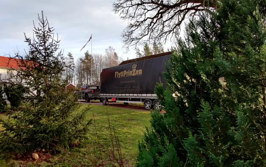En flyttbil med släp står parkerad på en uppfart till en villa. 