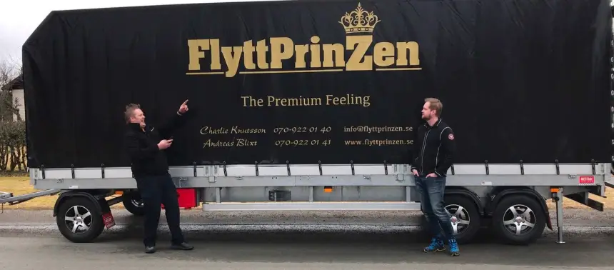 Två män står bredvid en flyttbil. Den ena pekar på loggans på bilens sida.
