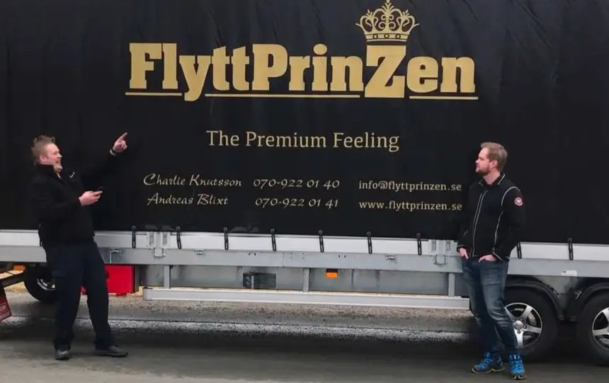 Två personer står vi en flyttbild med en logga i guld tryckt på sidan.